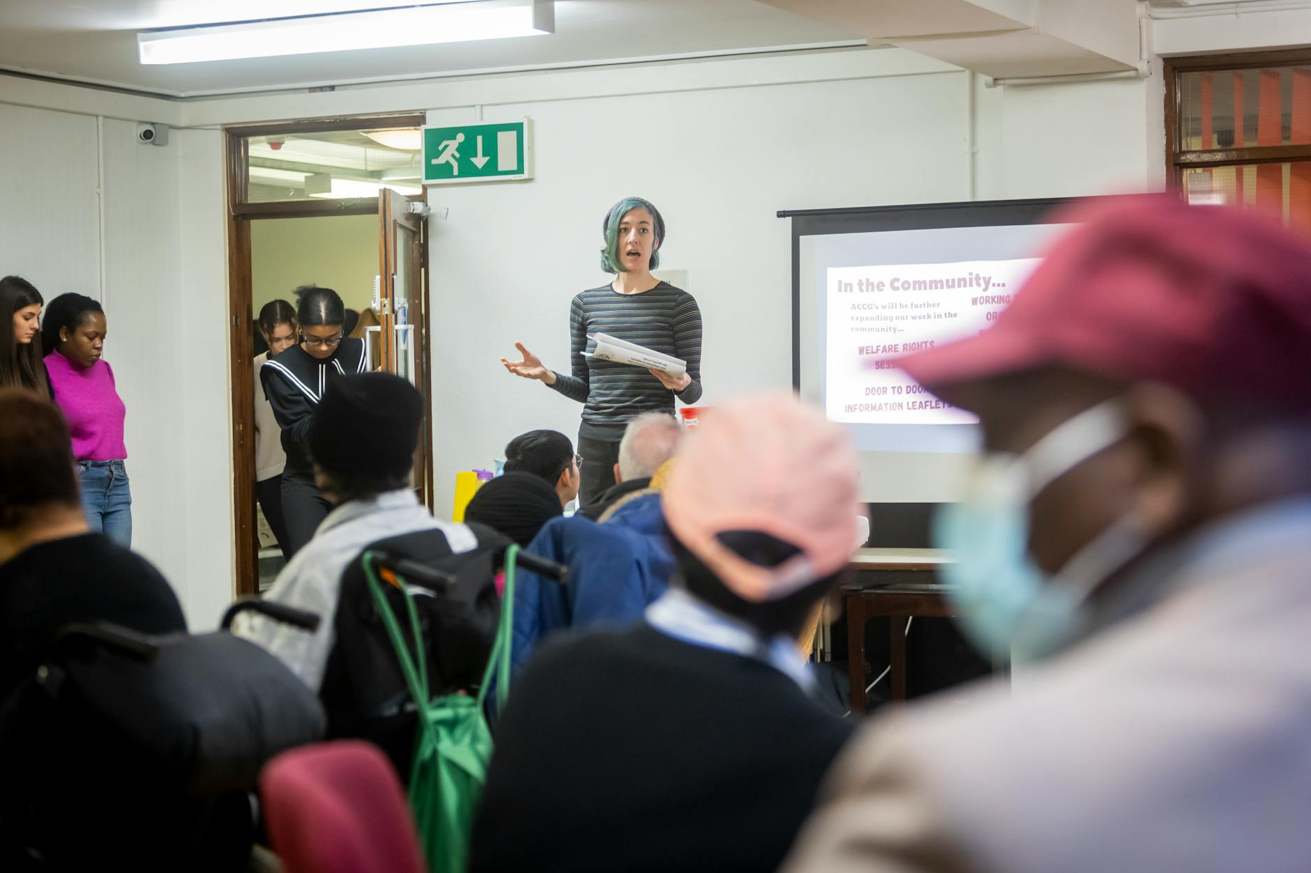 A diverse group attending a community meeting with a presenter speaking in front of a screen.