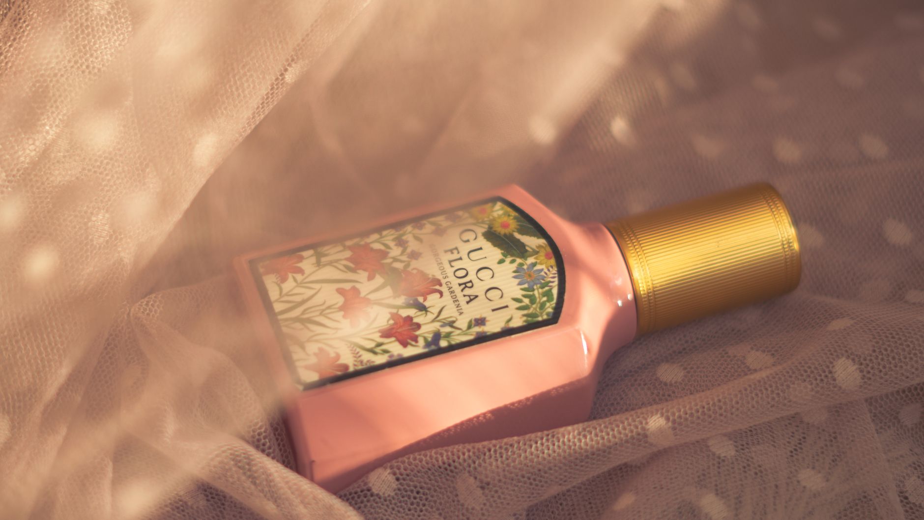 A close-up of a Gucci Flora perfume bottle surrounded by delicate fabric in warm lighting.